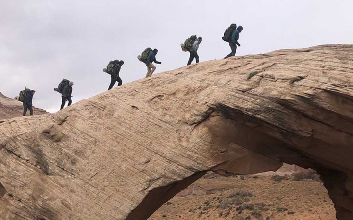 a group of gap year students hike over an arch in the american southwest